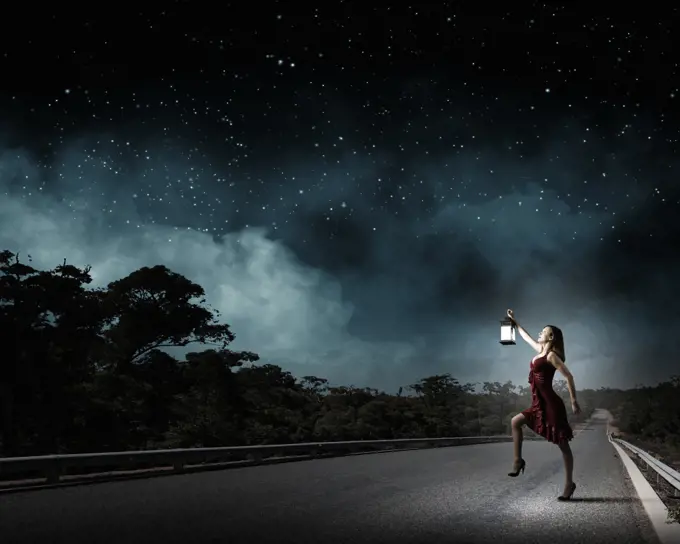 In search of something. Young attractive woman in red dress with lantern walking in darkness