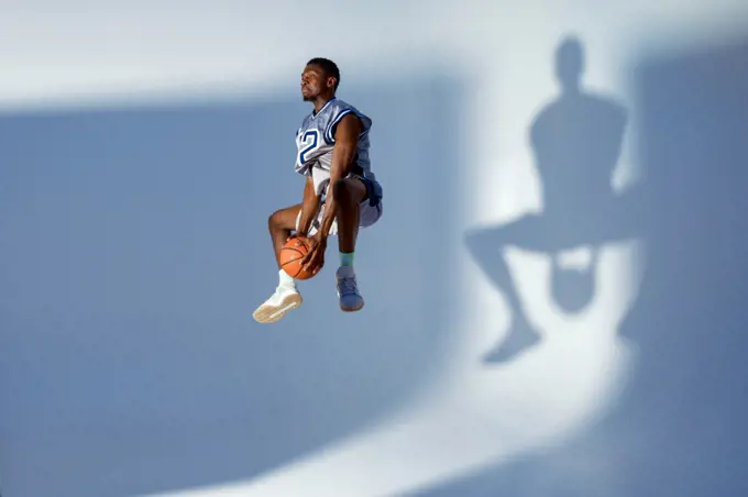 Basketball player with ball shows his skill in studio, high jump in action, neon background. Professional male baller in sportswear playing sport game, tall sportsman. Basketball player with ball, high jump in action