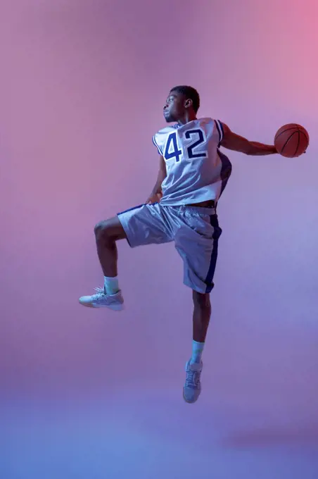 Basketball player jumping with ball in studio, neon background. Professional male baller in sportswear playing sport game. Basketball player jumping with ball in studio