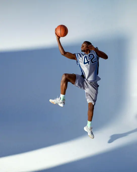 Basketball player with ball shows his skill in studio, high jump in action, neon background. Professional male baller in sportswear playing sport game, tall sportsman. Basketball player with ball, high jump in action