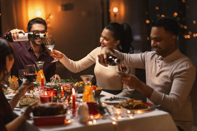 holidays, party and celebration concept - multiethnic group of happy friends having christmas dinner at home and drinking wine. happy friends drinking wine at christmas party