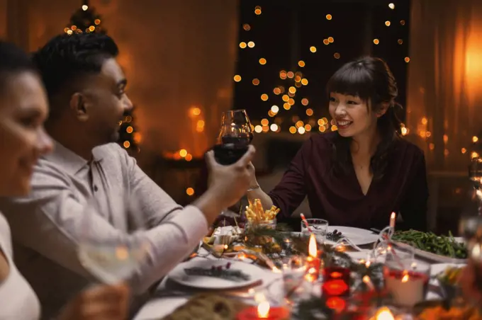 holidays, party and celebration concept - multiethnic group of happy friends having christmas dinner at home and drinking wine. happy friends drinking wine at christmas party