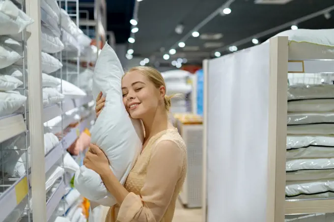 Smiling satisfied woman customer holding downy pillow buying goods in home textile shop boutique. Smiling woman customer buying pillow in shop