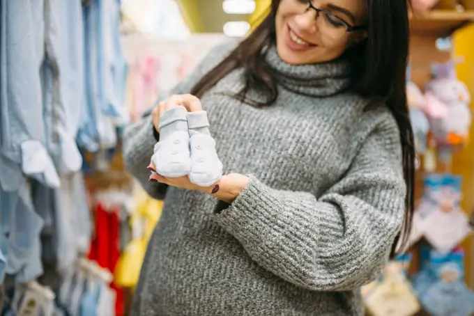 Happy future mother buys childrens clothes in the store for newborns. Pregnant woman in shop of goods for infants. Happy future mother buys childrens clothes