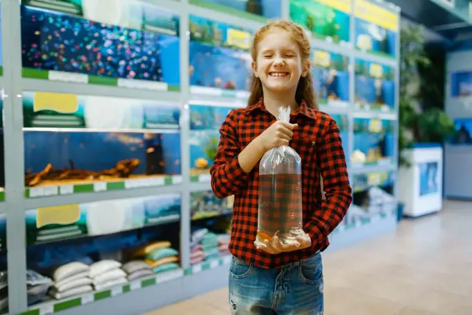 Happy little girl holds goldfish and makes a wish, pet store. Child buying equipment in petshop, accessories for domestic animals. Girl holds goldfish and makes a wish, pet store