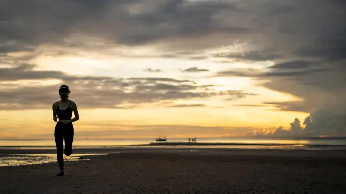 Woman in sportswear jogging on beach in the morning.