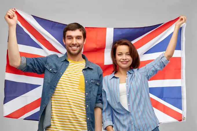 patriotism and national concept - happy couple holding british flag over grey background. happy couple holding british flag