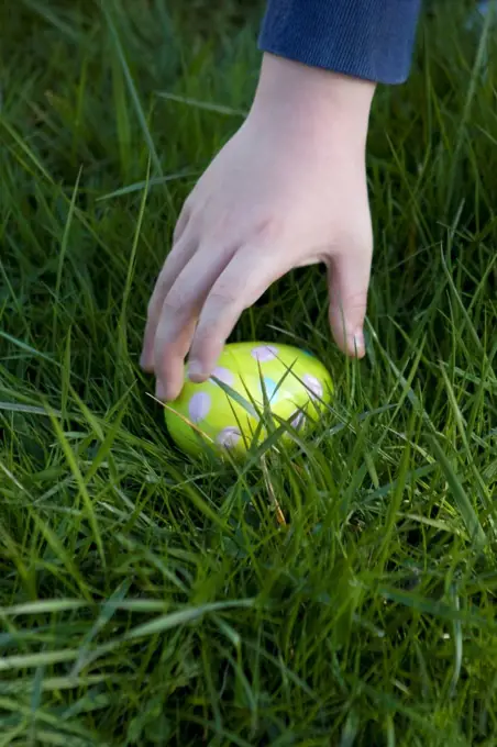 Child&acute;s hand about to pick up an Easter egg hidden in the grass