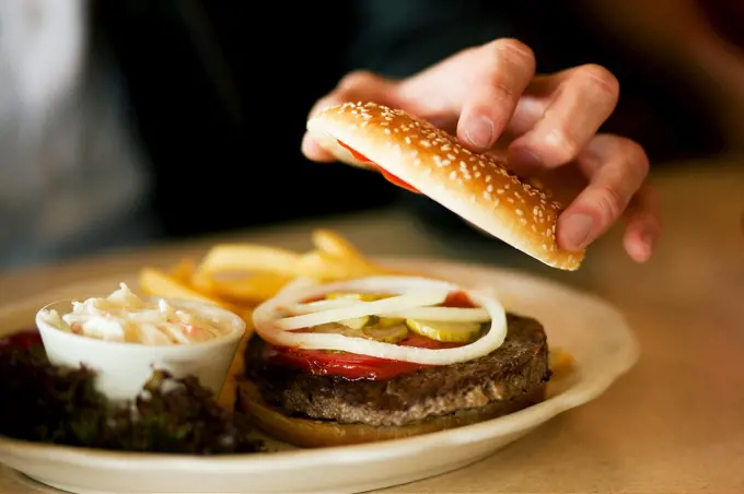 Man in a restaurant or diner eating a hamburger opening it to look inside, shot with available light, very selective focus