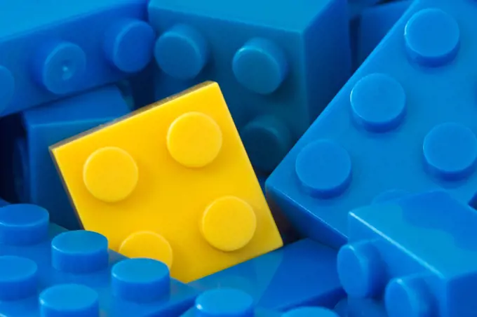 color toy background. yellow plastic brick in a middle of blue ones