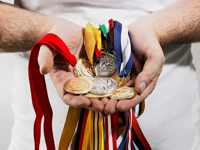 Mature man holding gold medals against white background