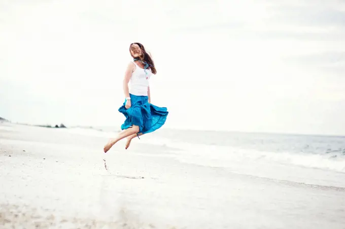 Young beautiful woman in white cami and turquoise skirt has fun on the ocean shore