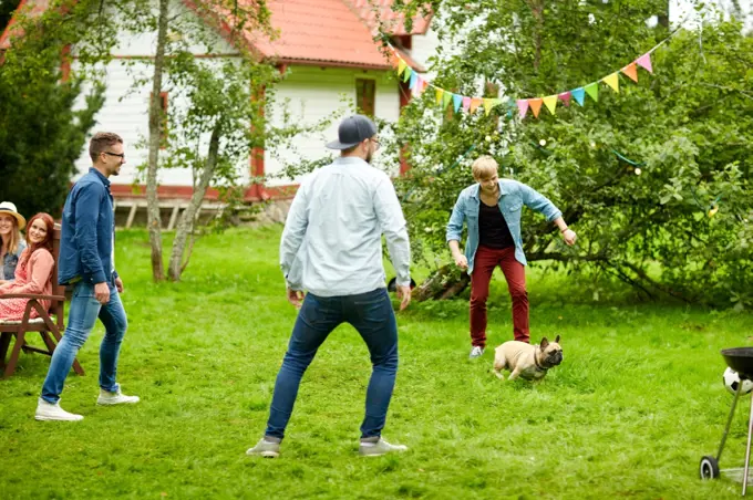 leisure, holidays, people and pets concept - happy friends playing with dog at summer garden party