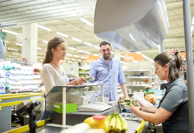 shopping, sale, consumerism and people concept - happy couple buying food at grocery store or supermarket cash register and paying cash money to cashier . couple buying food at grocery store cash register