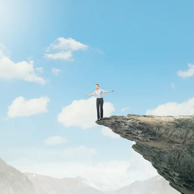 Risky business. Young businesswoman balancing on edge of hill top