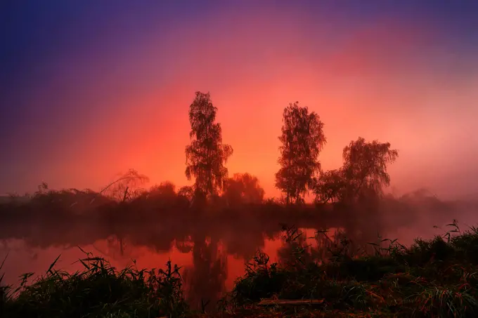 Autumn colorful sunrise on the foggy calm river. Autumn misty morning. Autumn dawn scene panorama.