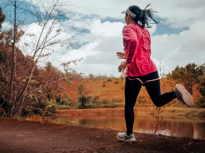 Athletic woman running on forest trail by the lake. Female runner running in nature in the morning. Workout Healthy lifestyle concept.