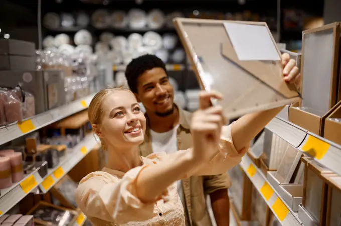 Young couple buying picture photo frame at shop. Multi ethnic woman man choosing decor for housing. Young couple buying photo frame at shop