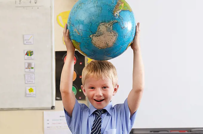 School boy holding globe over his head in a classroom