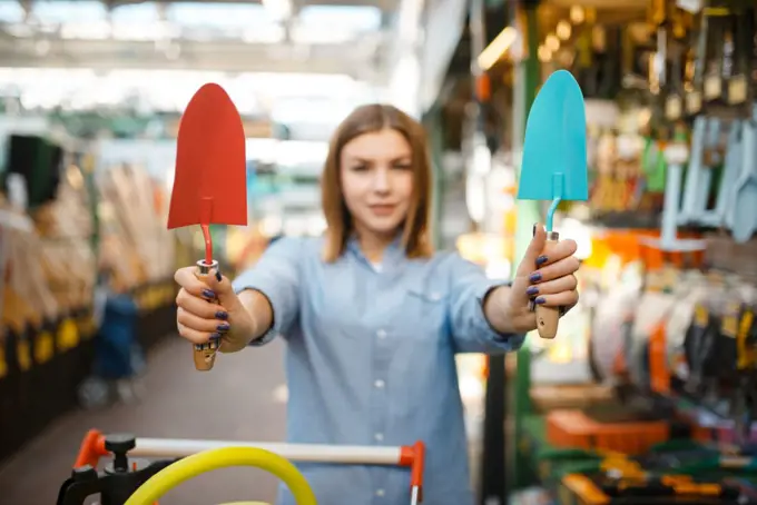 Female customer choosing garden shovel in shop for gardeners. Woman buying equipment in store for floriculture, florist instrument purchasing. Customer choosing garden shovel, gardeners shop