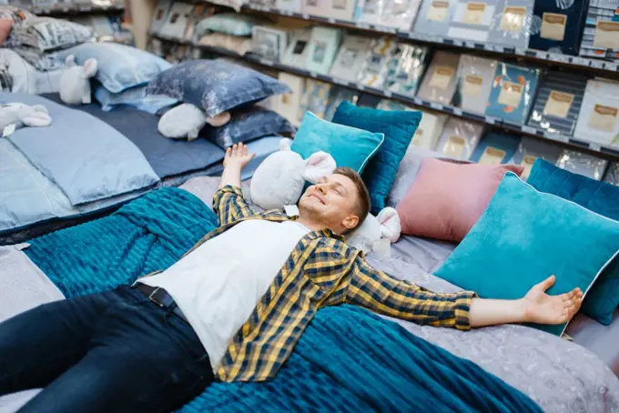 Young man lying on the bed in bedding store. Male person buying home goods in market, guy sleeping in shop. Young man lying on the bed in bedding store