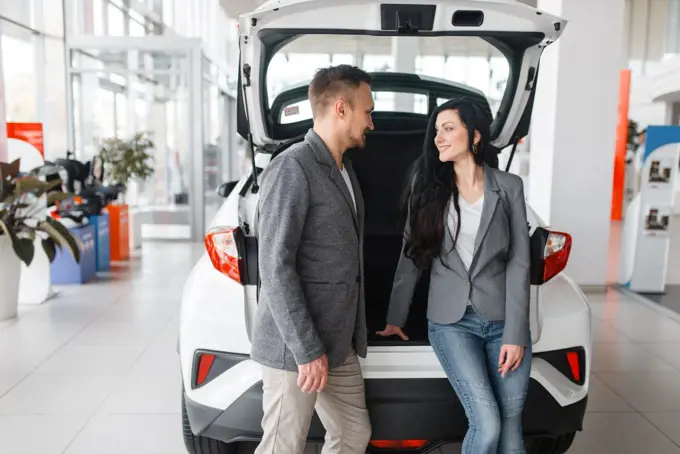 Couple buying new car in showroom, man and woman near the opened trunk. Male and female customers choosing vehicle in dealership, automobile sale, auto purchase