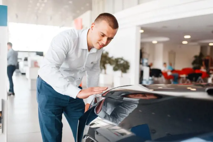 Manager checks the quality of new car paintwork in showroom. Male customer buying vehicle in dealership, automobile sale, auto purchase