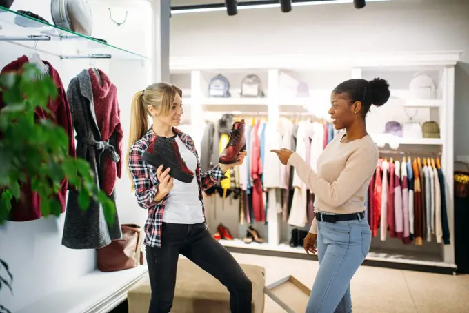 Two females buying clothes and shoes, shopping. Shopaholics in clothing store, consumerism lifestyle, fashion