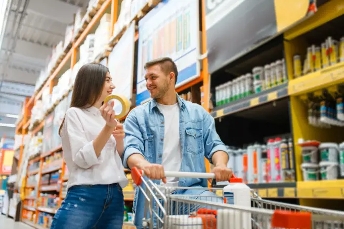 Couple with a cart buying building materials in hardware store. Customers look at the goods in diy shop. Couple with a cart buying building materials