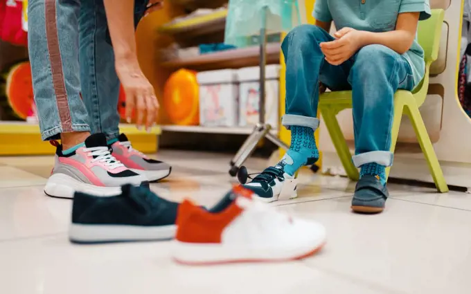 Mother with her little children choosing shoes in kids store. Happy mom with daughter and son buying clothes in supermarket together, family shopping. Mother with children choosing shoes in kids store