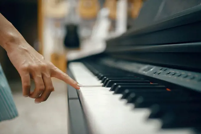 Young woman choosing digital piano in music store. Assortment in musical instrument shop, female musician buying equipment. Young woman choosing digital piano in music store