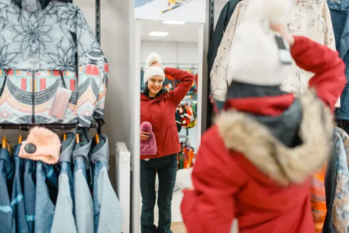 Woman at the showcase choosing skiing or snowboarding equipment, shopping in sports shop. Winter season extreme lifestyle, active leisure store, customer buying ski suit