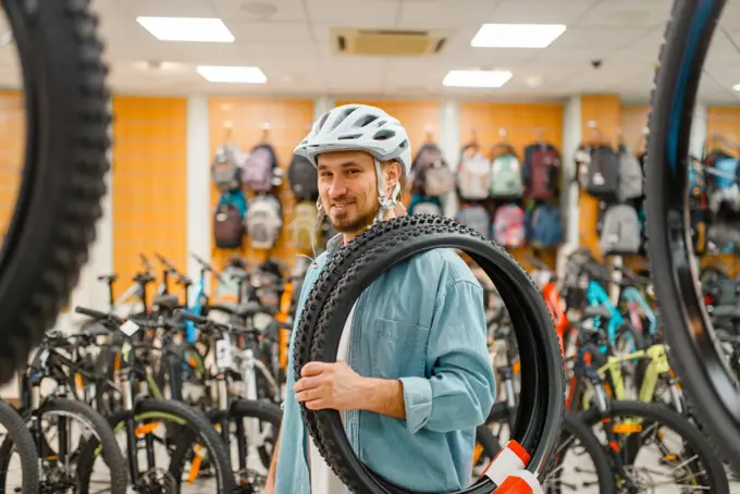 Man in cycling helmet holds bicycle tyres, shopping in sports shop. Summer season extreme lifestyle, active leisure store, customers buying bike equipment. Man in cycling helmet holds bicycle tyre, shopping