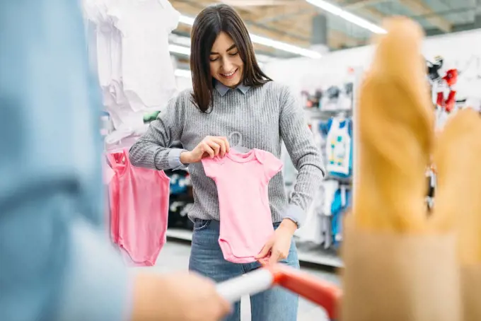 Young mother buying childrens clothes in store, family shopping. Customers in shop, buyers in market, department of goods for kids