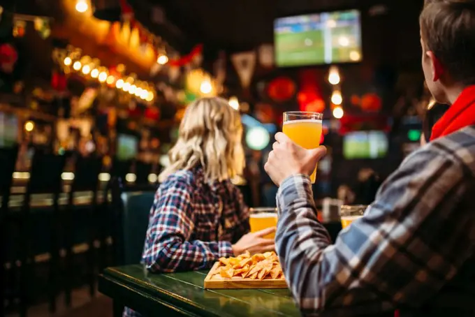 Football fans watching match and drinks beer at the table in sports bar. Tv broadcasting, young friends leisures in the pub. Fans watching match and drinks beer in sports bar