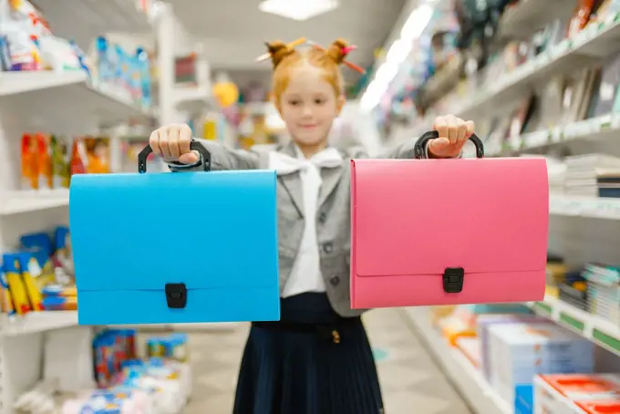 Little school girl with two folders in stationery store. Female child buying office supplies in shop, schoolchild in supermarket