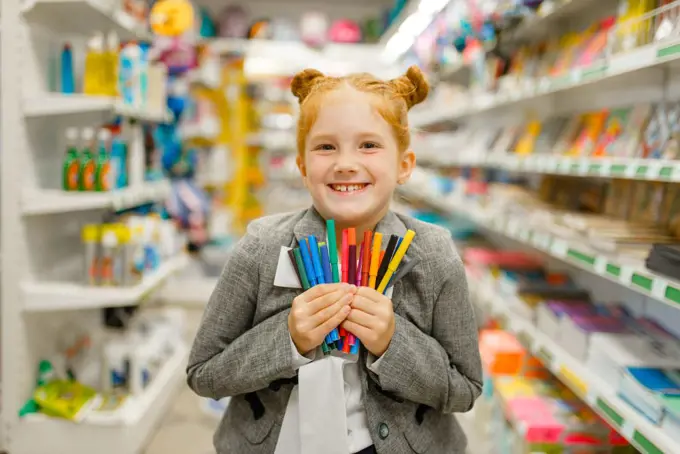 Little school girl holds colorful markers, shopping in stationery store. Female child buying office supplies in shop, schoolchild in supermarket. School girl holds markers, stationery store