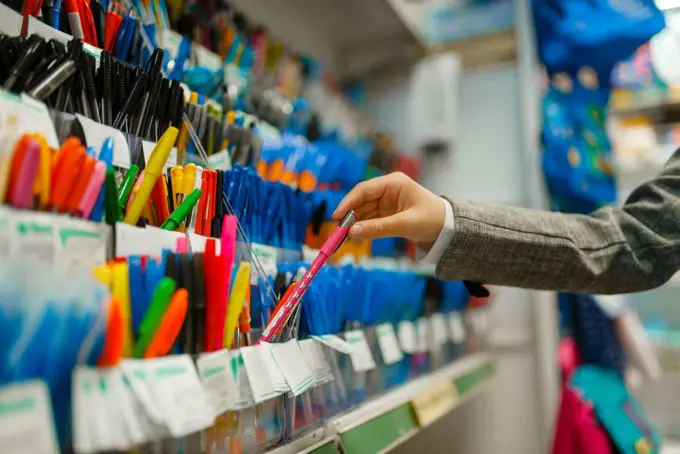 School girl choosing a pen at the shelf in stationery store. Female child buying office supplies in shop, schoolchild in supermarket