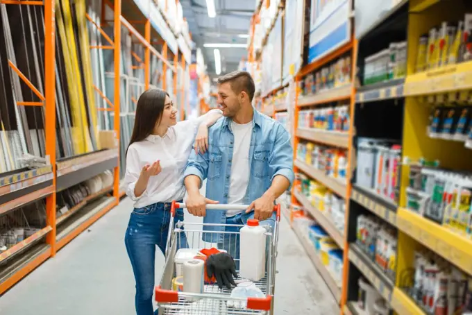 Couple with a cart buying building materials in hardware store. Customers look at the goods in diy shop