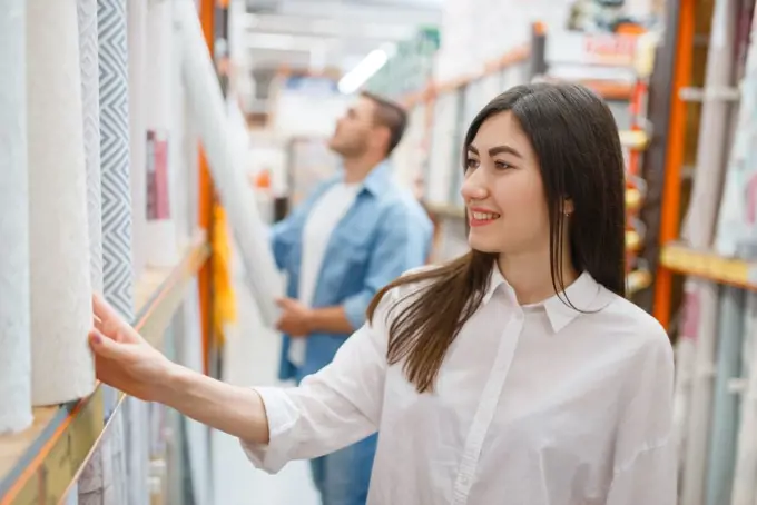 Young couple buying wallcovering in hardware store. Male and female customers look at the goods in diy shop. Young couple buying wallcovering in hardware store