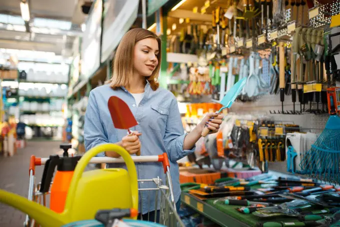 Female consumer choosing garden shovel in shop for gardeners. Woman buying equipment in store for floriculture, florist instrument purchasing. Consumer choosing garden shovel, gardeners shop