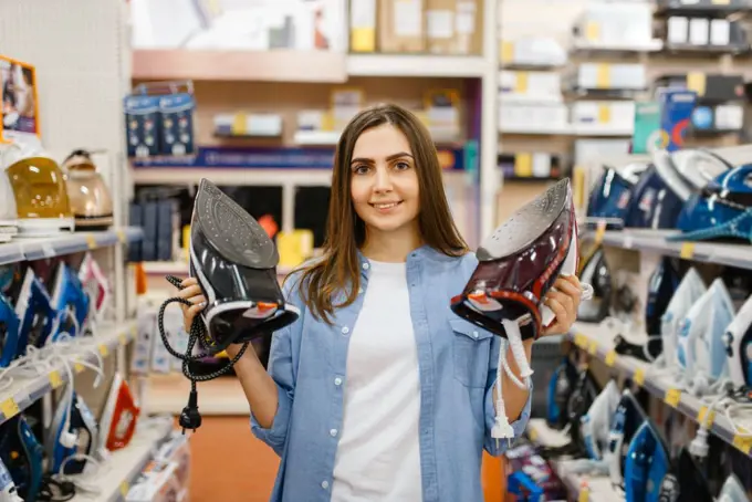 Woman choosing electric iron in electronics store. Female person buying home electrical appliances in market. Woman choosing electric iron in electronics store