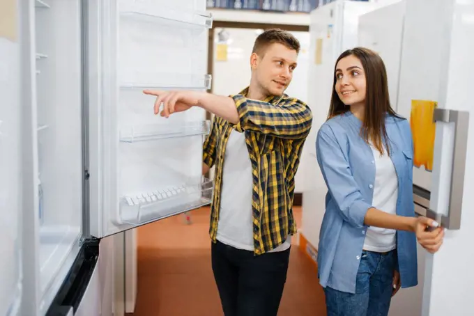 Young family couple choosing refrigerator in electronics store. Man and woman buying home electrical appliances in market. Young couple choosing refrigerator in store