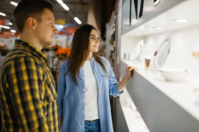 Young couple choosing wineglasses in houseware store. Man and woman buying home goods in market, family in kitchenware supply shop. Couple choosing wine glasses in houseware store