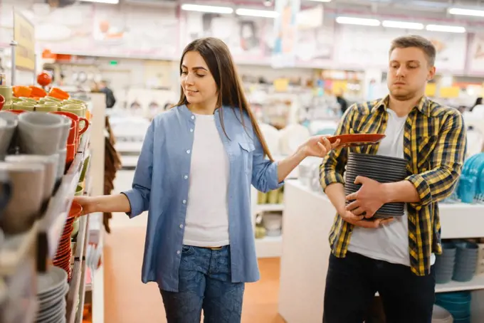 Young couple choosing plates in houseware store. Man and woman buying home goods in market, family in kitchenware supply shop. Young couple choosing plates in houseware store