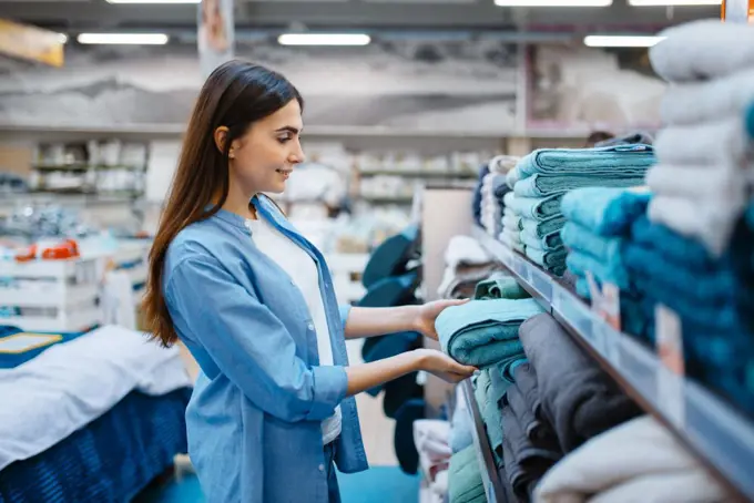 Young woman choosing towel in bed linen store. Female person buying home goods in market, lady in bedding shop. Young woman choosing towel in bed linen store