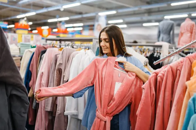 Young woman choosing bathrobe in bed linen store. Female person buying home goods in market, lady in bedding shop. Young woman choosing bathrobe in bed linen store