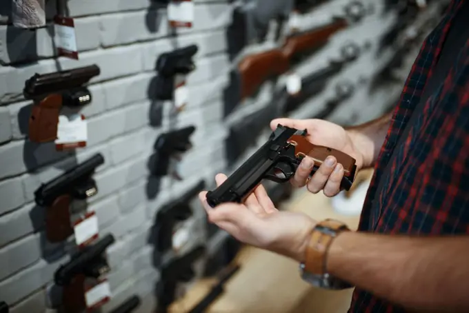 Man holds handgun in gun shop. Male person buying pistol for security in weapon store, selfdefence and sport shooting hobby. Man holds handgun in gun shop