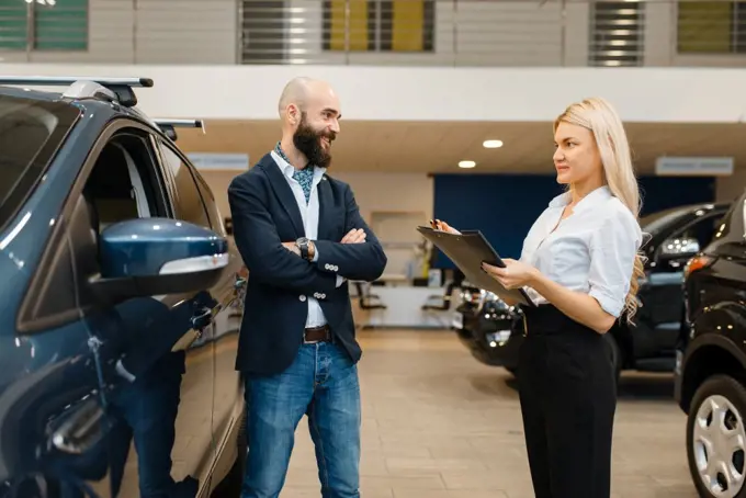 Smiling man and saleswoman in car dealership. Customer and seller in vehicle showroom, male person buying transport, auto dealer business. Smiling man and saleswoman in car dealership