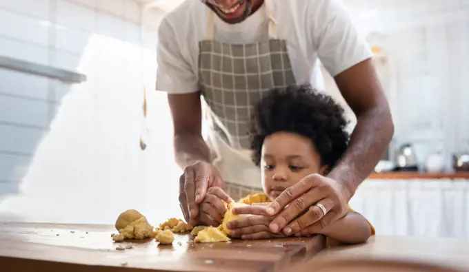 Black family having fun prepare bakery together at home. African American father and adorable son kneading dough in kitchen. Happy loving Man and little helper boy enjoy while making cakes and cookies